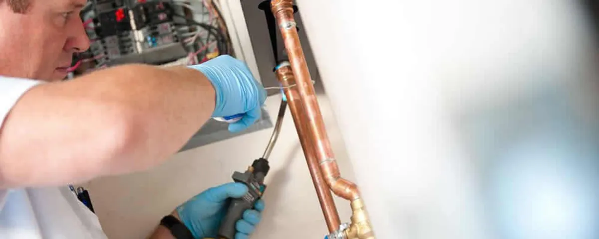Water heater repair technician testing copper pipe connections and controls in Olathe, KS