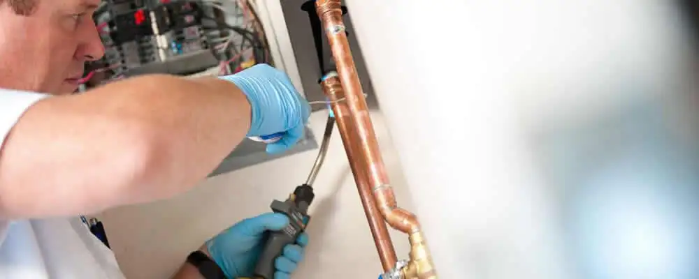 Water heater repair technician testing copper pipe connections and controls in Olathe, KS